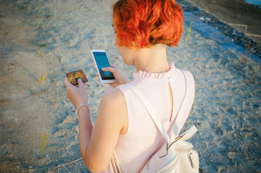 girl with red hair walking by the river at sunset, to make payments for online purchases from your device using a bank debit card. online payments, bank transfers.