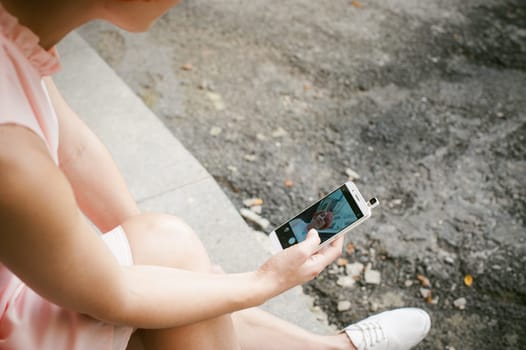 portrait of a girl doing selfie. girl in light pink dress with red dyed hair, pictures of themselves on their mobile camera phone, sitting on the stairs summer day