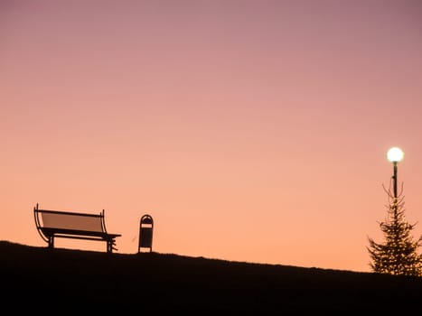 Silhouette of a bench with Christmas tree in the backlight of the sunset in East Frisia.