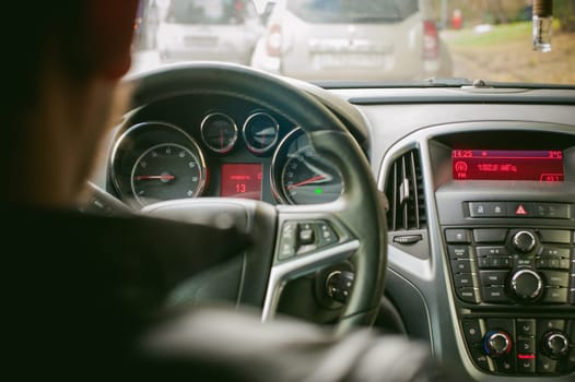 man drives a car. A guy in a jacket sits behind the wheel of a car traveling on the road in a traffic jam. Photo taken off the seat, due to the driver's back