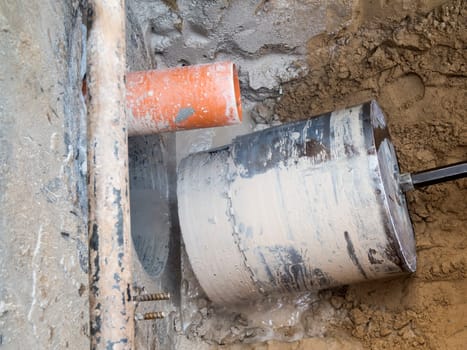 View of a finished core hole borehole with drill bit and drill core in a dug trench in front of a concrete wall.