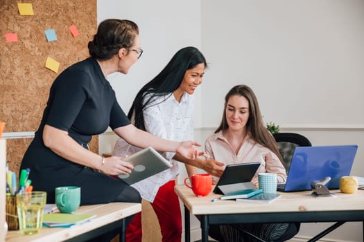 Women are working together in an office. They are talking as they use digital tablets.