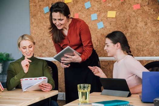 Women are working together in an office. They are talking as they use digital tablets.