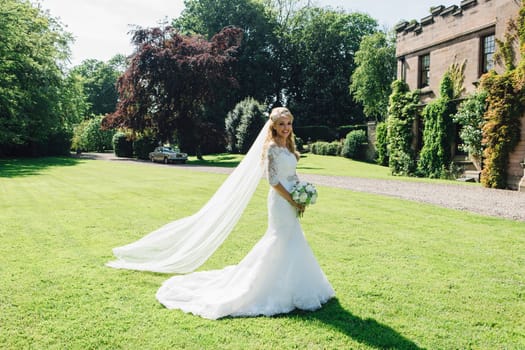 Beautiful bride is posing for the camera in her wedding dress in a formal garden.