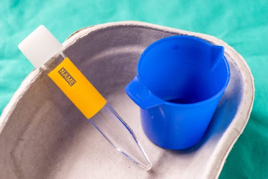 Medical test tube for urine sample lying in a one use capsule on the hospital's green background. The background can be a textile part of a doctor or nurse's work uniform