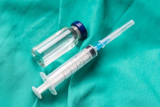 Medical syringe and vials lying on the hospital's green background. The background can be a textile part of a doctor or nurse's work uniform
