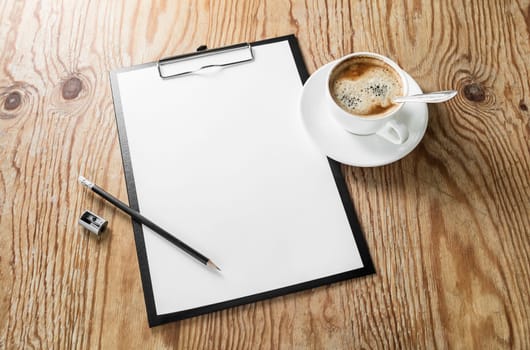 Photo of clipboard with a blank sheet of paper, coffee cup, pencil and sharpener on wooden background with plenty of copy space. Blank template for design presentations and portfolios. Responsive design mockup.