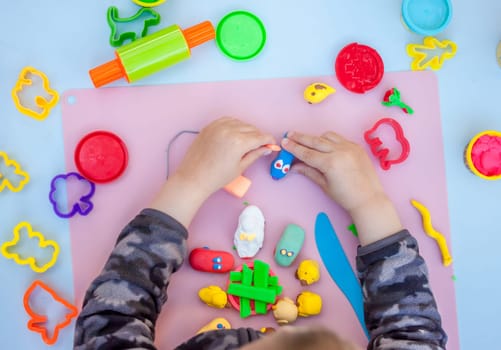 child hands playing with plasticine on blue table top view
