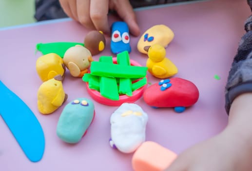 child hands playing with plasticine on blue table top view