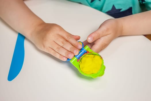 child hands playing with plasticine on blue table top view