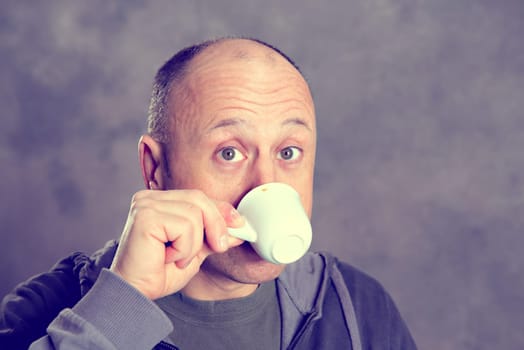 young baldheaded man drinking coffee in front of gray background