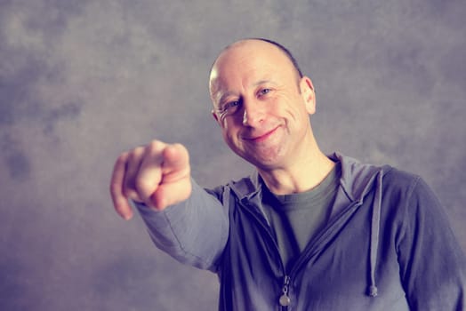 young baldheaded man in front of gray background pointing in to the camera