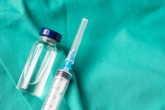 Medical syringe and vials lying on the hospital's green background. The background can be a textile part of a doctor or nurse's work uniform