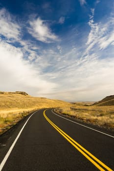 A well preserved two lane road leads around a bend to an interesting sky