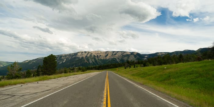 A well worn two lane road leads to a vanishing point in the mountains