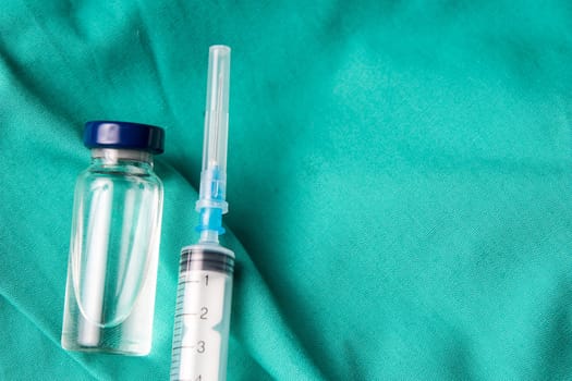 Medical syringe and vials lying on the hospital's green background. The background can be a textile part of a doctor or nurse's work uniform