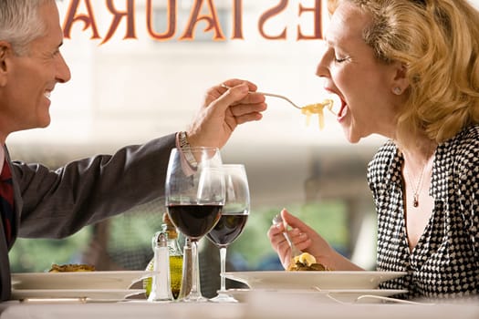Man feeding pasta to woman