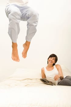 Woman watching husband jump on bed