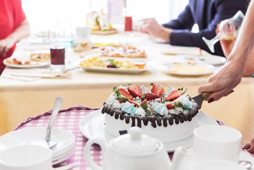 Tasty strawberry cream cake on checkered table, with tea set
