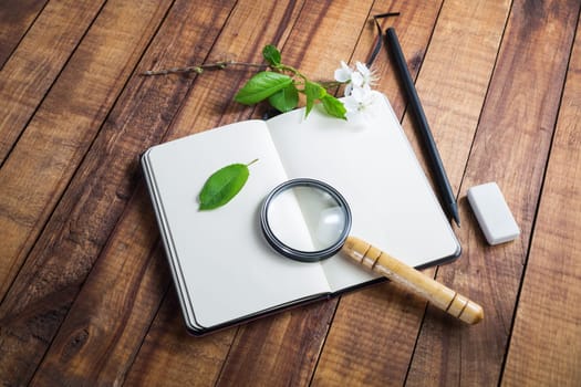 Blank opened notebook, magnifier, pencil and eraser on wooden background. Photo of stationery elements. Template for placing your design. Responsive design mockup.