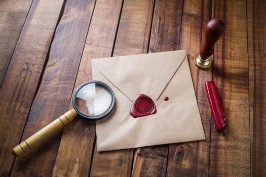Envelope, magnifier, seal, stamp on wood table background. Responsive design mockup. Vintage still life with postal accessories. Blank stationery.