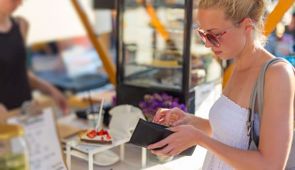 Beautiful blonde caucasian lady wearing white summer dress buying freshly prepared meal at a local street food festival. Urban international kitchen event in Ljubljana, Slovenia, in summertime.