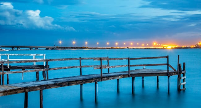 Long exposure of an old jetty on a river with city lights in the background