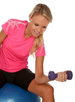 Pretty blonde girl sitting on an exercise ball while lifting weights
