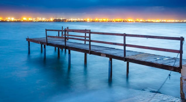 Long exposure of an old jetty on a river with city lights in the background