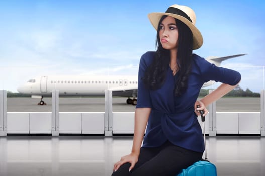 Portrait of asian traveler woman with unhappy face sitting on suitcase in the airport
