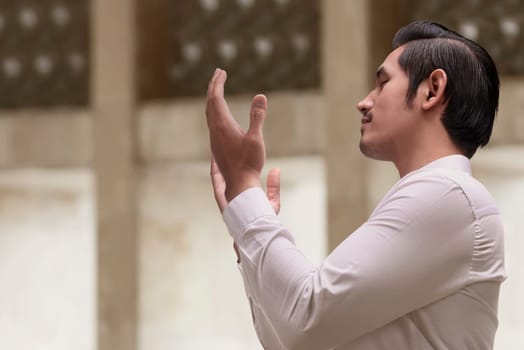 Religious asian muslim man in traditional dress praying in the mosque