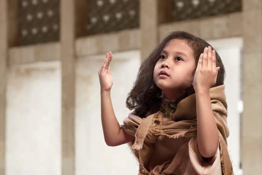 Cute asian muslim child in traditional dress praying on the mosque