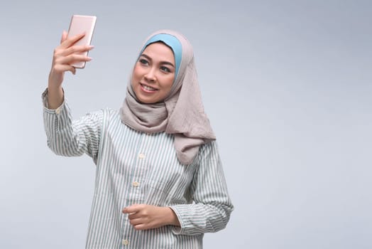 Young asian muslim woman posing talking selfie with mobile phone over dark background