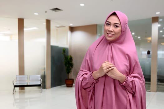 Happy asian muslim woman in traditional veil standing at office
