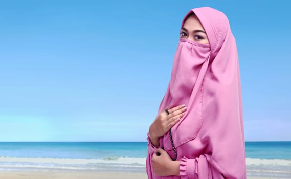 Portrait of asian muslim woman with niqab holding prayer beads on the beach