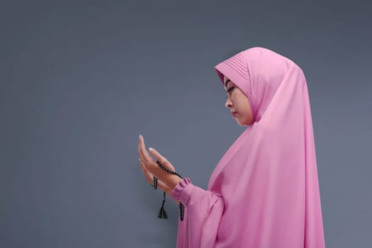 Beautiful asian muslim woman with hijab praying to god against dark background