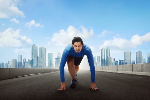 Sporty asian man runner getting ready for running on road with cityscape background