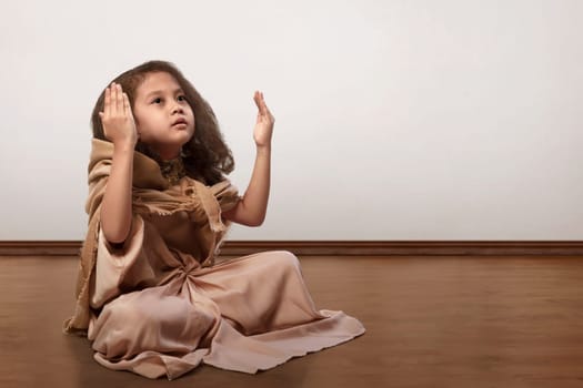 Portrait of asian muslim kid sitting on floor and praying inside the room
