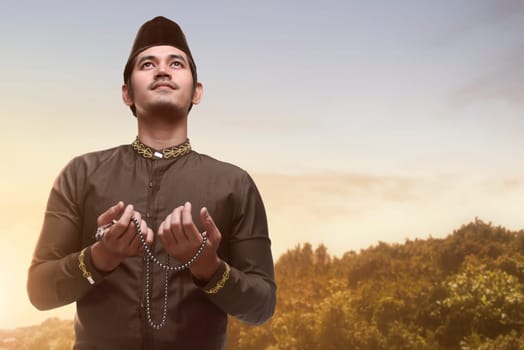 Handsome asian muslim man holding prayer beads and praying during sunset