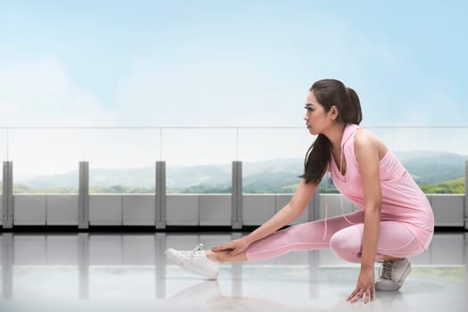 Portrait of asian woman in sportswear doing stretching while kneeling in front of window at gym