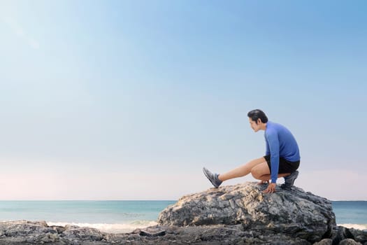 Portrait of asian fitness man stretching legs before jogging on the beach