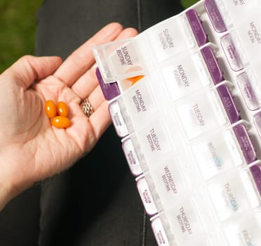 Pills are poured into hand from the daily weekly medication planner holder