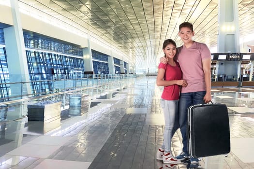 Smiling asian couple holding luggage bags to traveling at airport