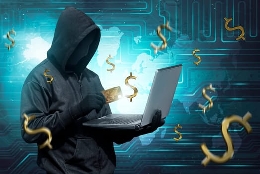 Hacker man with mask holding credit card with laptop on his hand on digital background