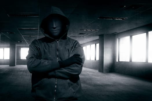 Hooded man with mask standing alone in the empty dark room