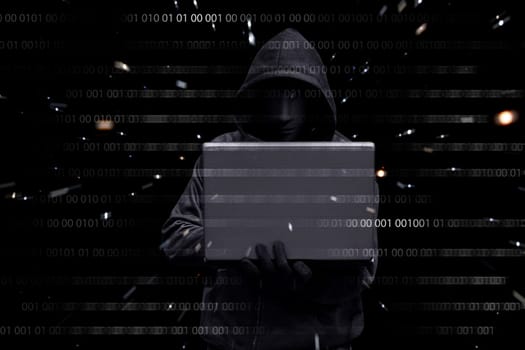 Hacker with anonymous mask typing on a laptop against binary code in background