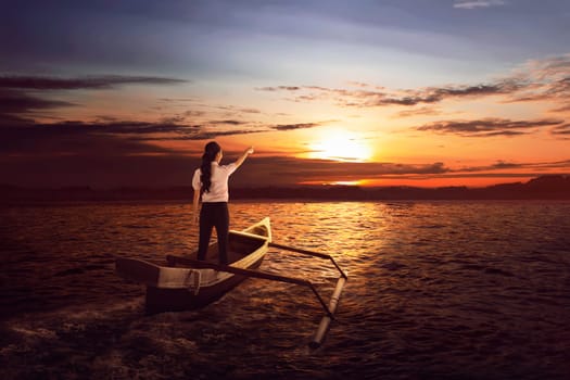 Beautiful asian business woman standing and pointing to the sun on the boat at sunset