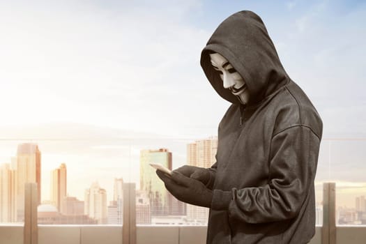 Hacker with mask using smartphone to steal data on the office