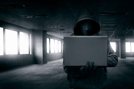 Hacker with mask using laptop on the empty dark room