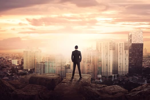 Young asian businessman standing looking at the city from the edge of rock mountain